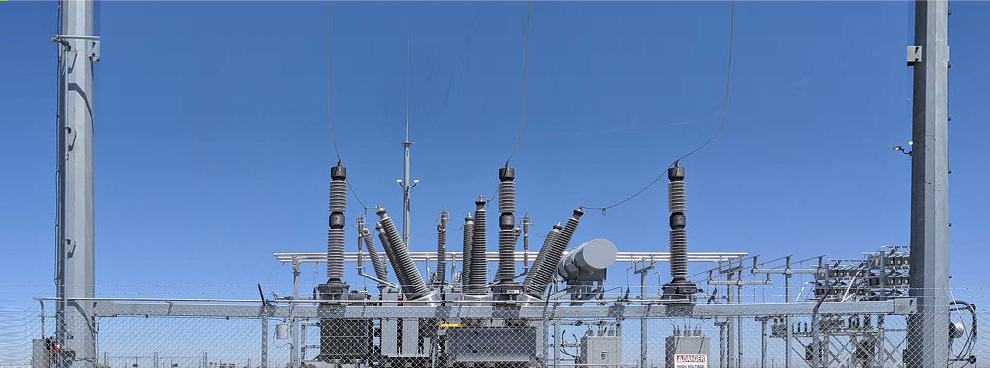 photo of a high voltage substation behind a fence with a blue sky backround