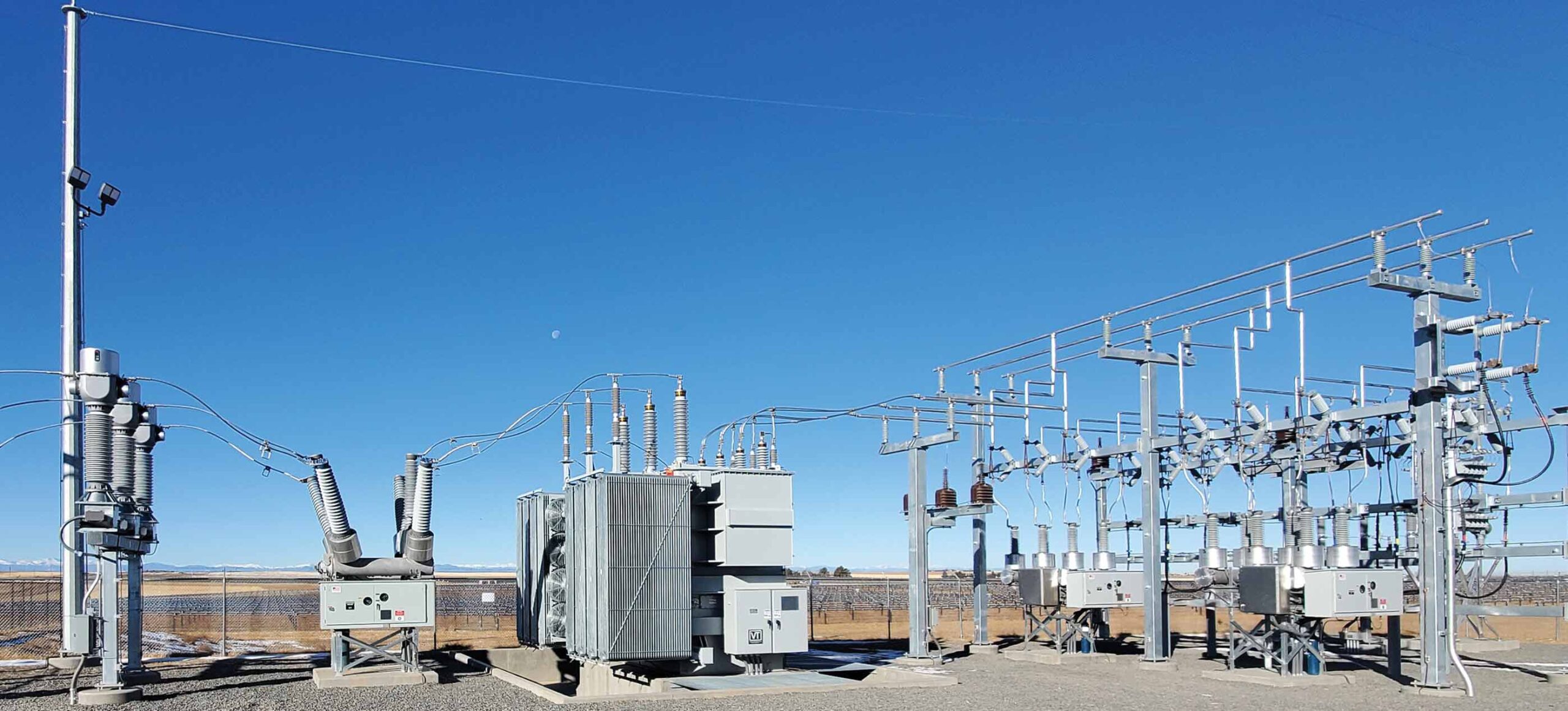 photo of a high voltage substation behind a fence with a blue sky backround