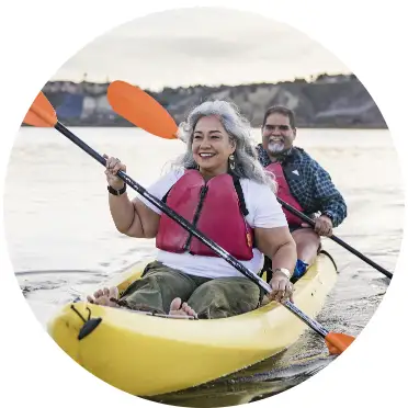 A grey-haired woman and grey-bearded man paddling in a kayak and smiling